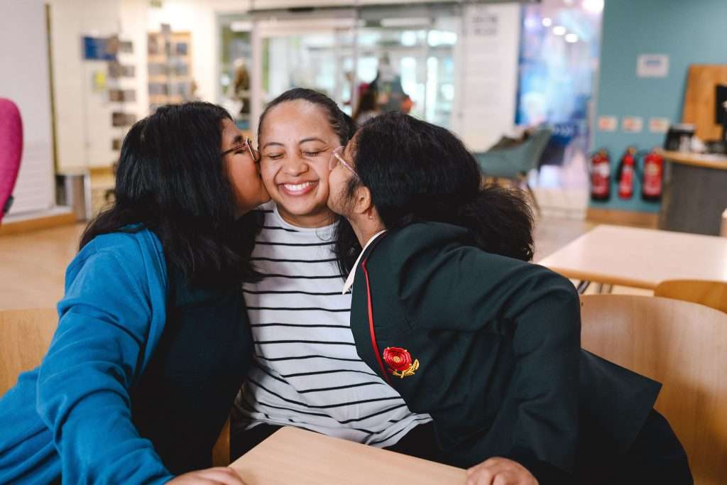 Two young girls giving their mum a kiss on the cheek