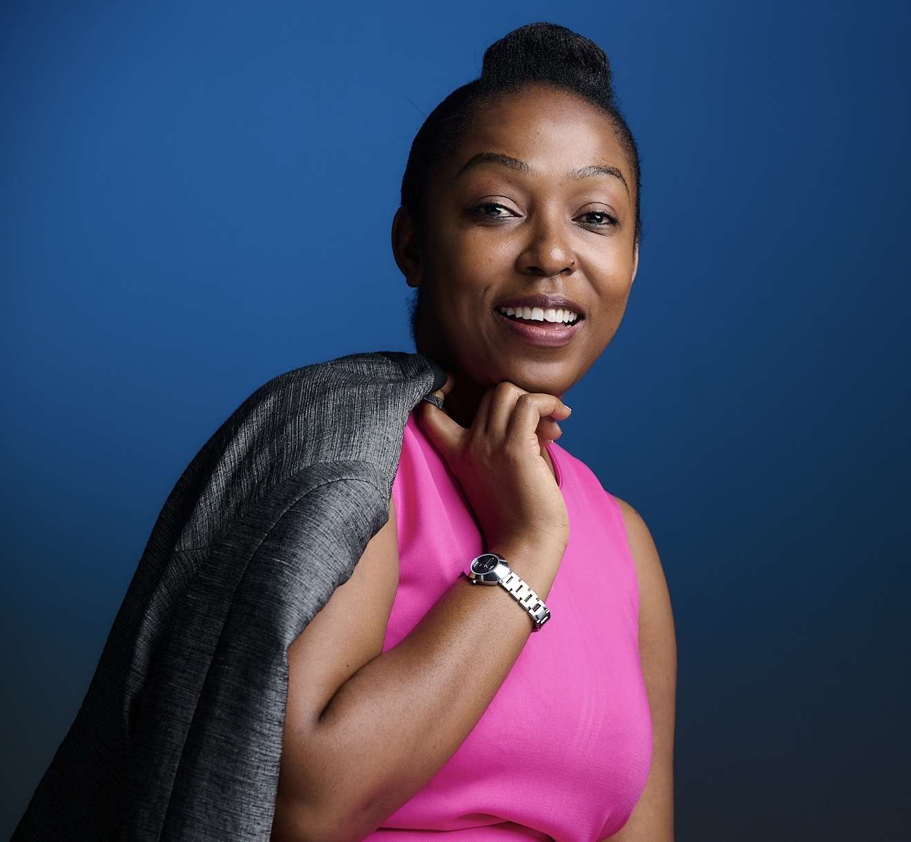 A young black woman smiling at a camera holder a jacket over her shoulder